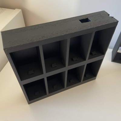 Organizador preto de madeira com oito compartimentos, visto de cima, sobre mesa branca.