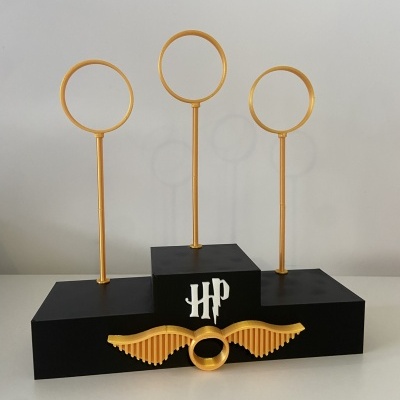 Suporte em blocos preto com argolas douradas e detalhes decorativos de asas e letras HP