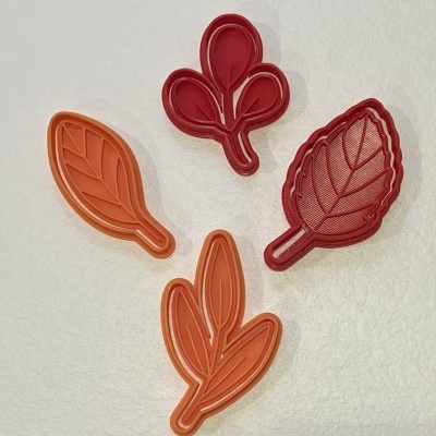 Conjunto de cortadores de biscoitos em formas de folhas e frutas em plástico vermelho e laranja.