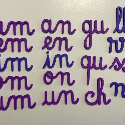 Letras cursivas padrão violeta e azul formando sílabas em superfície clara