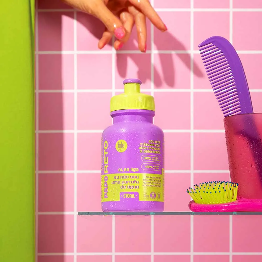 Frasco pequeno roxo com tampa amarela e texto em amarelo numa prateleira transparente com acessórios de pente e escova à direita