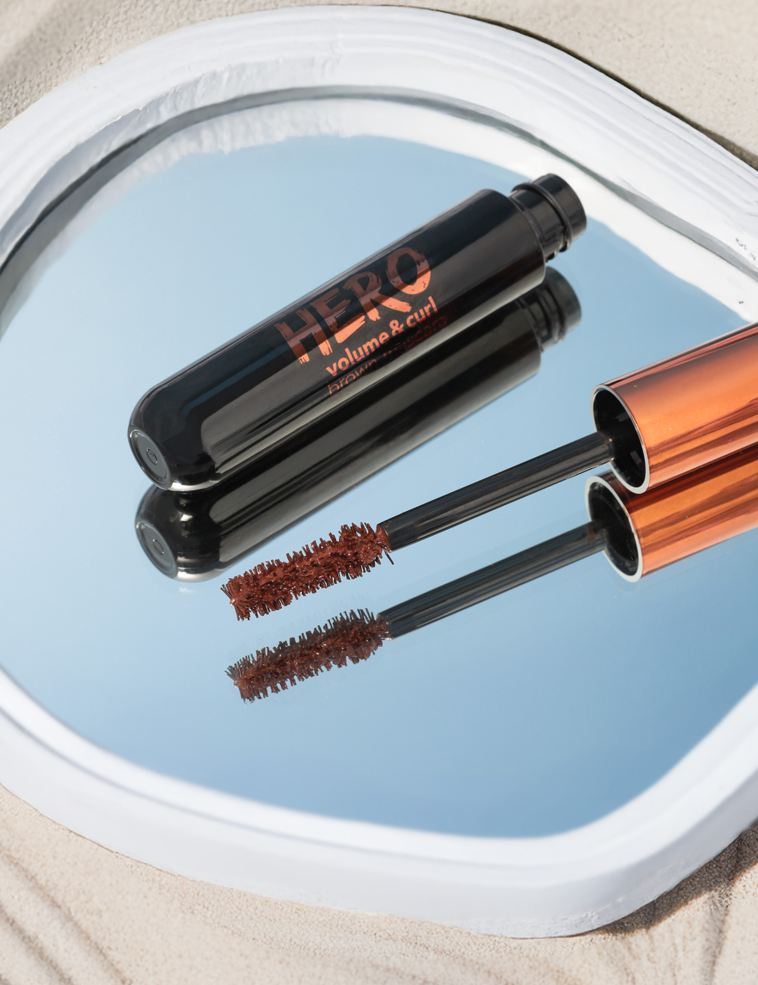 Máscara de pestanas HERO preto com tampa bronze refletida em espelho redondo
