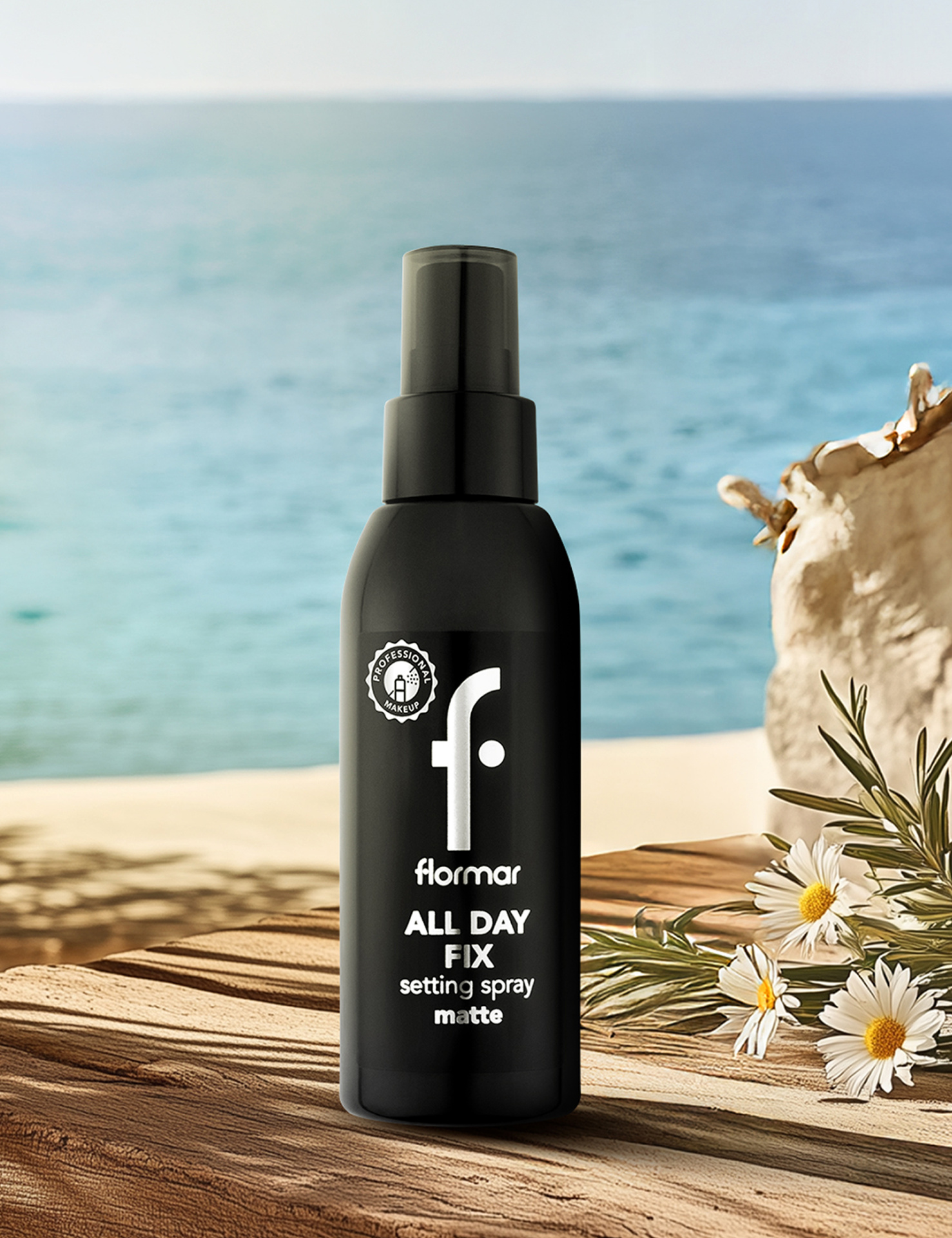 Frasco preto de spray fixador modelado mate da marca flormar em superfície de madeira com mar e flores ao fundo