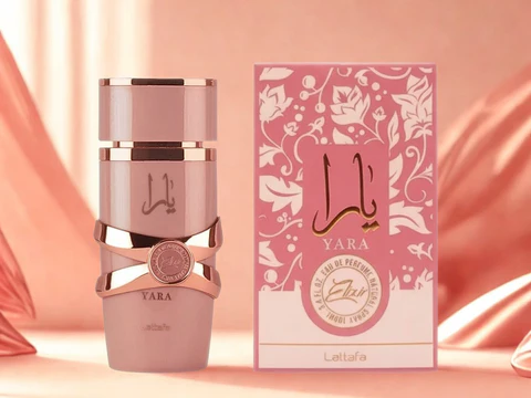 Frasco e caixa de perfume YARA rosa com detalhes dourados sobre fundo de tecido cor de salmão