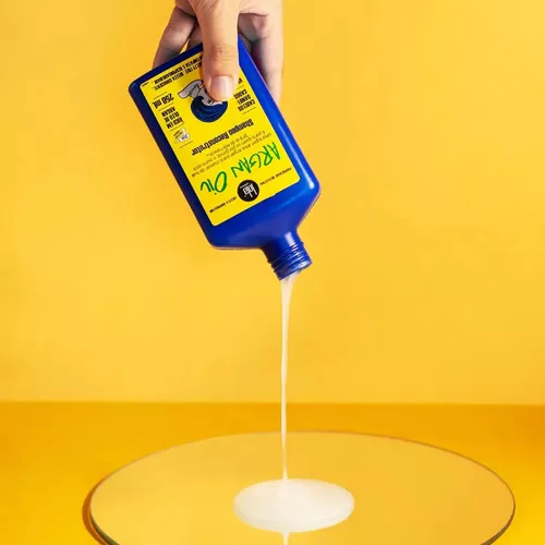 Óleo de rícino a ser vertido de garrafa azul com rótulo amarelo sobre superfície espelhada