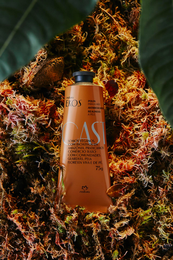 Embalagem laranja de creme Natura Ekos Castanha sobre musgo colorido