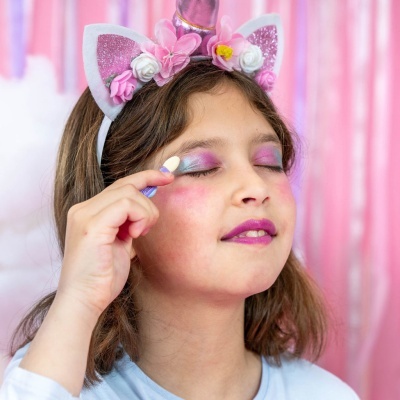 Menina com tiara de unicórnio rosa e branca a aplicar maquilhagem