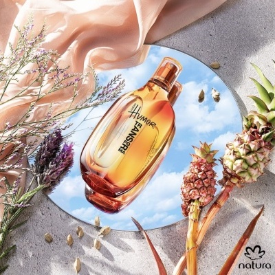 Perfume âmbar Humor refletido em espelho com flores secas e mini abacaxis em fundo cinza