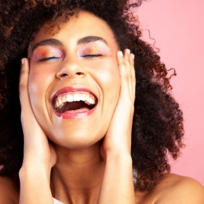 Mulher sorridente com maquilhagem rosada e cabelo encaracolado sobre fundo rosa