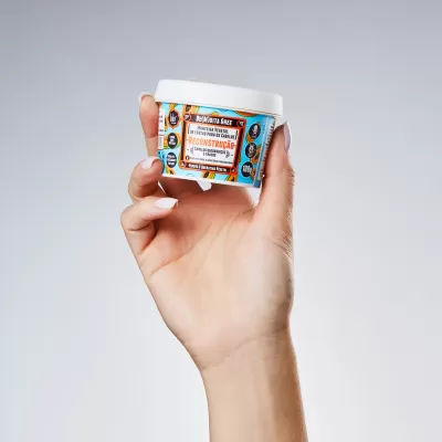 Mão a segurar embalagem branca com rótulo colorido de produto de cuidado