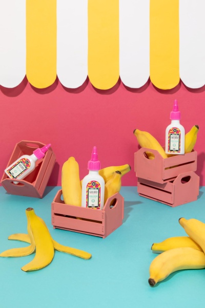 Mini caixas de madeira com bananas e frascos de cola branca em fundo colorido