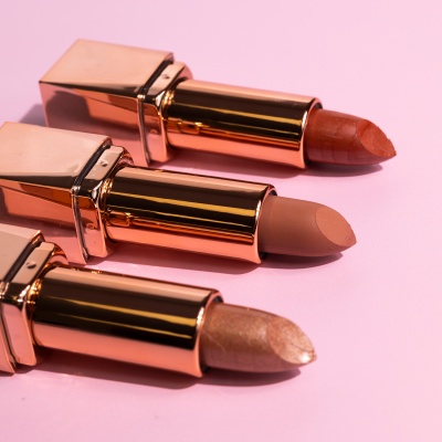 Três batons dourados de diferentes tons sobre fundo rosa