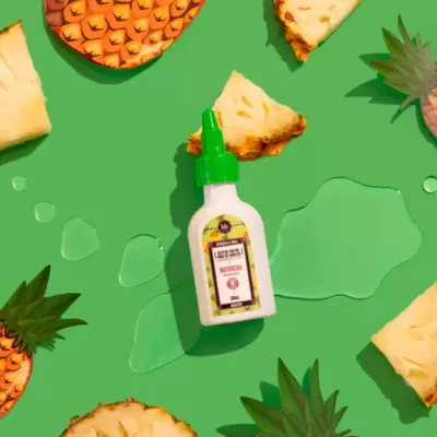 Frasco de cola com tampo verde rodeado por fatias de ananás em fundo verde