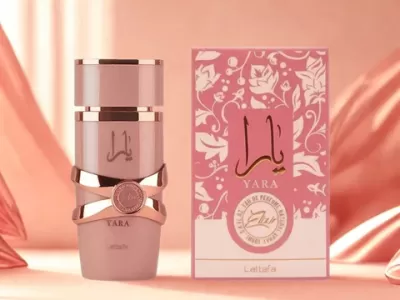 Frasco e caixa de perfume YARA rosa com detalhes dourados sobre fundo de tecido cor de salmão