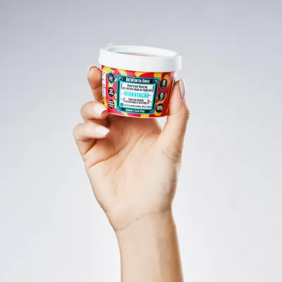 Mão segurando creme hidratante facial em frasco branco com rótulo colorido