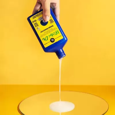 Óleo de rícino a ser vertido de garrafa azul com rótulo amarelo sobre superfície espelhada