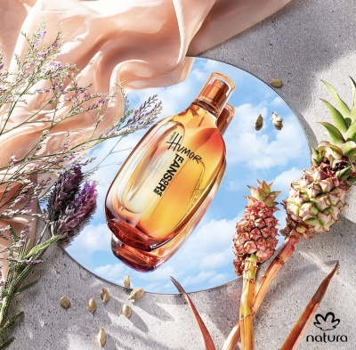 Perfume âmbar Humor refletido em espelho com flores secas e mini abacaxis em fundo cinza