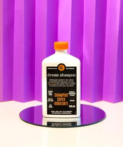 Frasco branco de shampoo com tampa laranja sobre espelho com fundo roxo