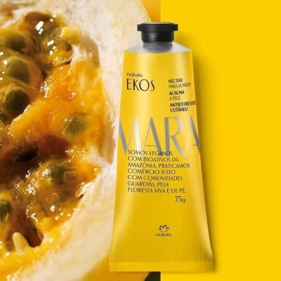 Tubo amarelo de creme para mãos Natura Ekos Mara com fruta aberta ao lado