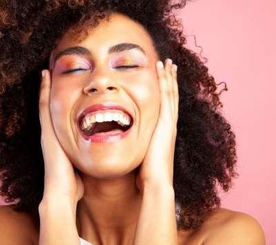 Mulher sorridente com maquilhagem rosada e cabelo encaracolado sobre fundo rosa