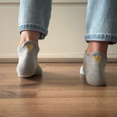 Meias cinzentas com coração amarelo usadas com jeans em chão de madeira