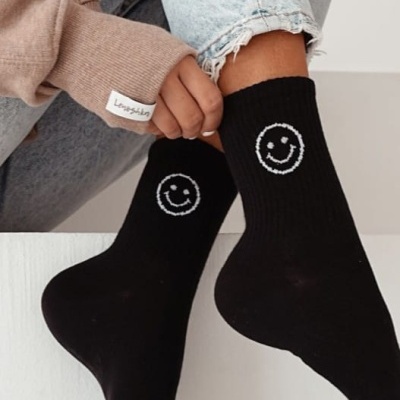 Meias pretas com rosto sorridente branco usadas com calças de ganga e camisola bege