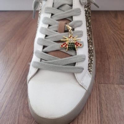 Ténis branco com cadarços cinza, risca dourada de lantejoulas e pendente abelha colorida