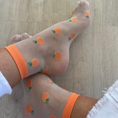 Meias transparentes com padrão de laranjas e acabamento laranja usadas com calças brancas