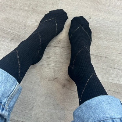 Meias pretas com padrão em zig-zag dourado usadas por pessoa com calças de ganga azul claro sobre chão claro