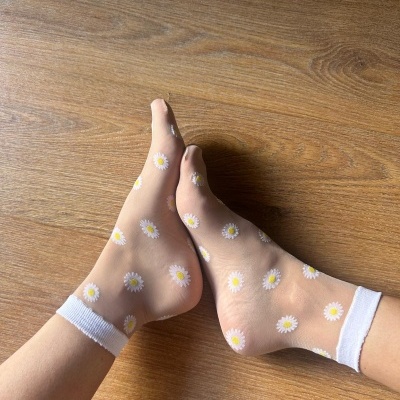 Meias transparentes com padrão de flores em pés sobre chão de madeira