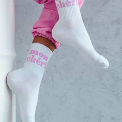 Meias brancas com texto 'mon chéri' em cor-de-rosa usadas por pessoa com calças cor-de-rosa
