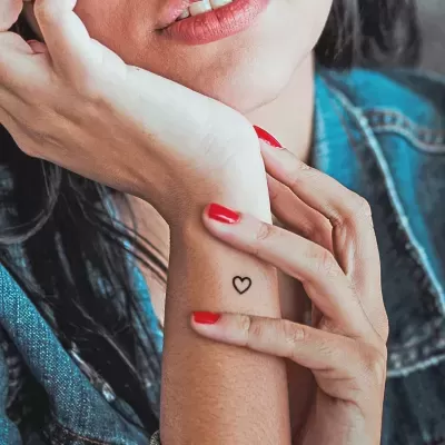 Pessoa com tatuagem de coração pequeno no pulso e unhas vermelhas