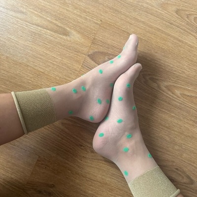 Meias transparentes com pontos verdes e punhos bege em piso de madeira clara