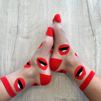 Meias transparentes com padrão de bocas vermelhas e pretas em chão de madeira