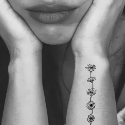 Braço com tatuagem de flores lineares pretas numa sequência vertical