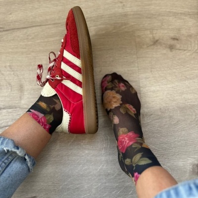 Meias transparentes pretas com padrão floral e sapatos desportivos vermelhos com riscas brancas em pavimento de madeira