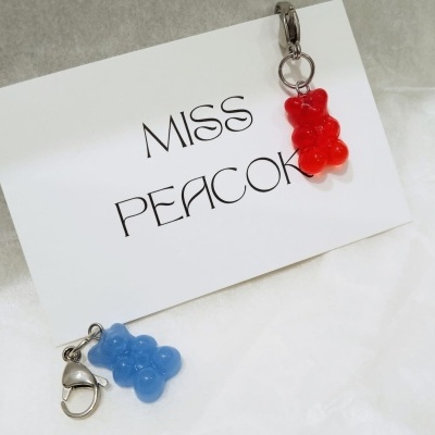 Porta-chaves com ursinhos vermelho e azul sobre cartão branco com texto MISS PEACOK.