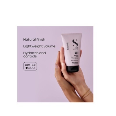 Tubo rosa claro de produto cosmético com tampa preta segurado por mãos femininas sobre fundo lilás claro