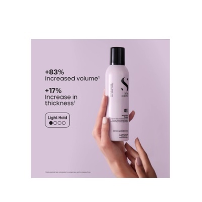 Lata rosa de spray para cabelo com texto em inglês sobre aumento de volume e espessura, segurada por uma mão, fundo lilás