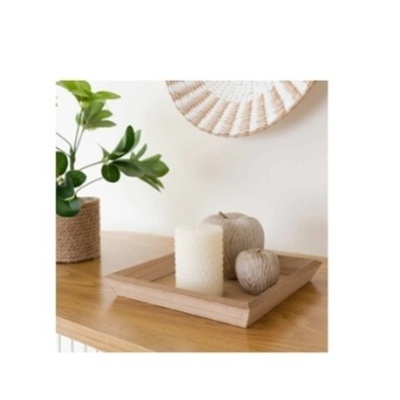 Tabuleiro de madeira com vela branca e objetos decorativos em forma de maçã sobre móvel de madeira com planta ao lado