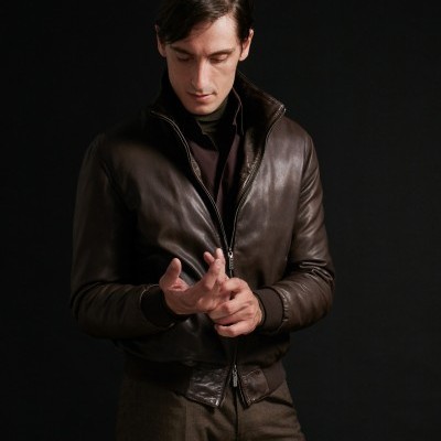 Homem com casaco de cabedal castanho escuro e calças castanhas frente a fundo preto