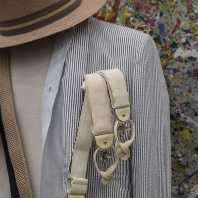 Manequim com casaco de riscas, mochila bege e chapéu de palha com fundo colorido