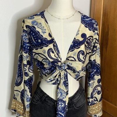 Blusa feminina azul e bege com padrão paisley e laço frontal no manequim