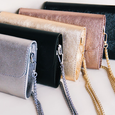 Cinco malas pequenas com correntes metálicas, várias cores e texturas brilhantes.