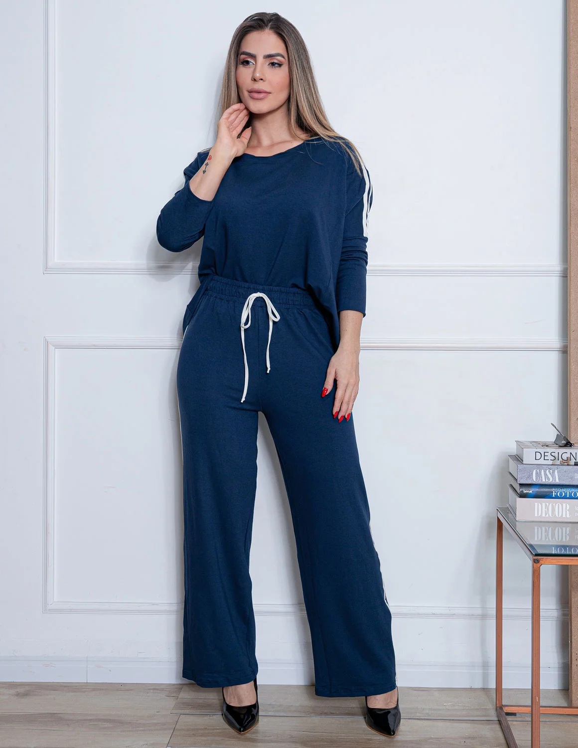 Conjunto Elegante em Viscose Premium com Calça Pantalona e Blusa de Manga Ajustada - Casual Chic Mulher com conjunto azul escuro de calças e camisa de mangas compridas em ambiente interior branco