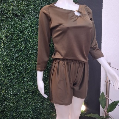 Conjunto de roupa castanho com blusa de mangas 3/4 e calção, manequim branco em fundo verde e planta.