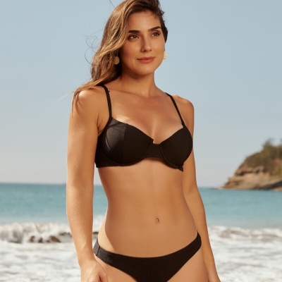 Mulher com biquíni preto texturizado na praia com mar e céu azul