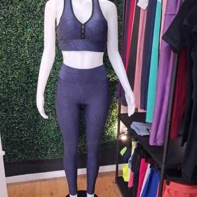 Conjunto desportivo azul escuro em manequim com padrão geométrico em relevo e parede verde ao fundo.