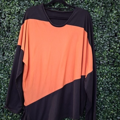Camisola preta e laranja de manga comprida pendurada num cabide sobre fundo verde de folhas
