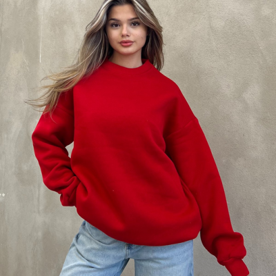 Mulher com sweatshirt vermelha e jeans contra parede cinzenta